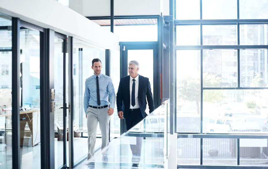 One older man walking down hallway with younger man